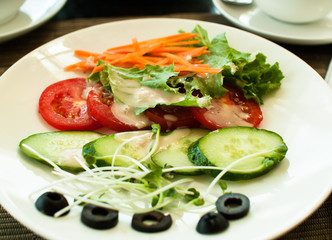 Plate with vegan fresh vegetables: tomatoes, cucumbers, olives, salad, carrots view from above