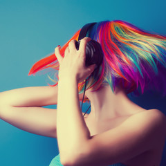 beautiful woman wearing colorful wig and headphones against blue