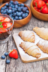 fresh croissants and berries with cup of fruit tea on old table