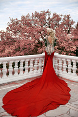 Fashion elegant blond woman model in red gown with long train of