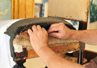 Upholsterer repairing the seat of a chair. Tapicero reparando el relleno del asiento de una silla