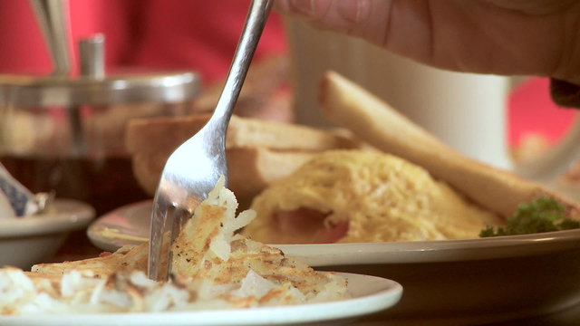 Close view of a diner's fork lifting up hash browns from a breakfast plate.