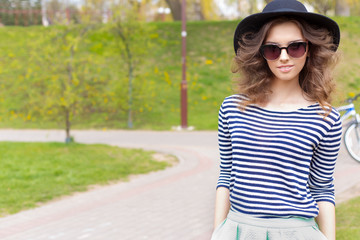 bright happy girl in hat and sunglasses walking in the park