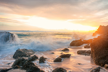 sunset seascape with rocky beach and crashing waves 
