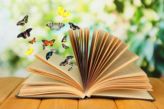 Open book on wooden table and butterflies on natural background