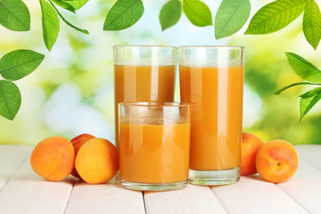 Glasses of apricot juice and fresh apricots on table on green background
