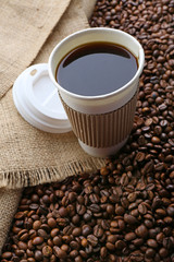 Paper cup of coffee with beans on sackcloth close up