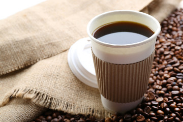 Paper cup of coffee with beans on sackcloth close up