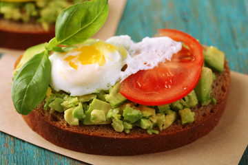 Fototapeta na wymiar Tasty sandwich with egg, avocado and vegetables on paper napkin, on color wooden background