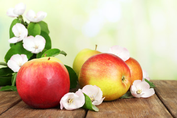 Fresh apples with apple blossom on wooden table, on nature background