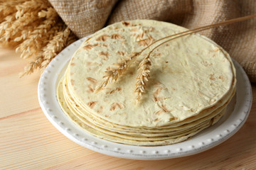 Stack of homemade whole wheat flour tortilla on plate, on wooden table background