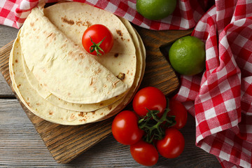 Stack of homemade whole wheat flour tortilla and vegetables on cutting board, on wooden table background