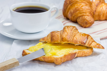 Fresh croissant with lemon curd and cup of coffee