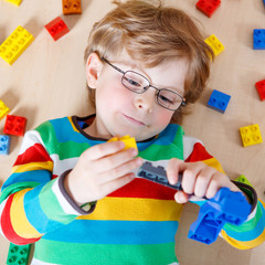Little blond kid boy playing with lots of colorful plastic block