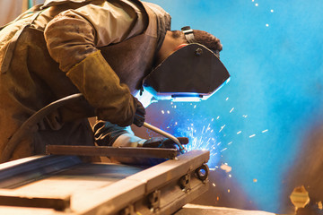 Young man welding inside in a factory