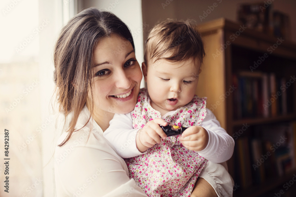 Wall mural Beautiful young mother holding her cute little daughter