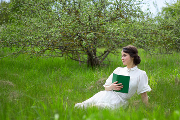 beautiful woman in white vintage dress with book on summer meado
