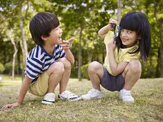asian children playing with magnifier outdoors