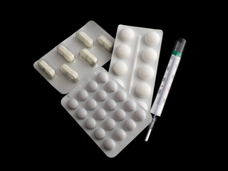 Pills and thermometer isolated on black background