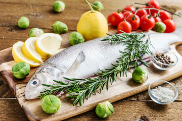 Fresh fish with vegetables and spices on wooden board