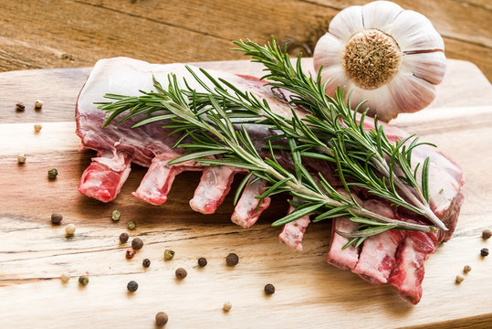 Raw lamb ribs with rosemary, pepper and garlic on wooden board
