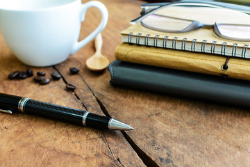 Close up of pen with notebook and cup of coffee on wooden table