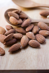 Almonds in spoon on brown wooden background