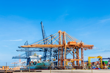 Cranes load containers on a large transport ship at trade port