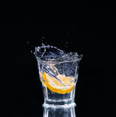 Slice of lemon splashing into a glass of water with a spray of water droplets