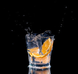 Slice of lemon splashing into a glass of water with a spray of water droplets 