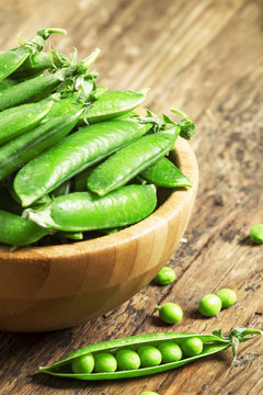 Pods of fresh green peas in a bowl on old wooden table, selectiv