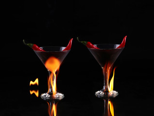 collage Hot chili pepper in a martini glass with a fire on a black background