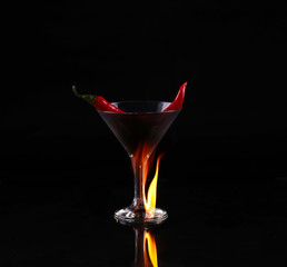 Hot chili pepper in a martini glass with a fire on a black background