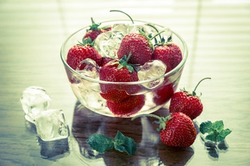 Fresh strawberries with ice cubes in the glass bowl