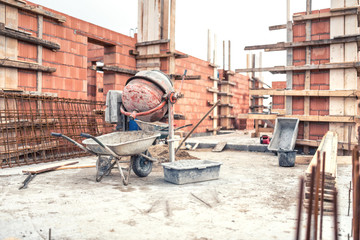 Cement mixer machine at construction site, tools, wheelbarrow