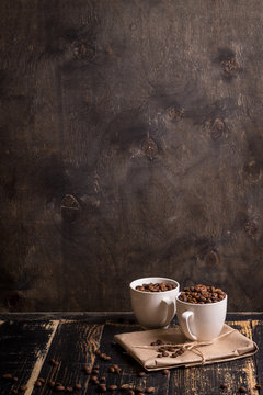 Fototapeta Cup with coffee beans at dark wooden background