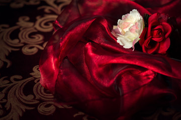 Two Silk flowers on Red Silk Material Background