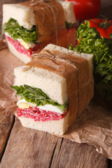 sandwiches with salami, lettuce and egg wrapped in paper 
