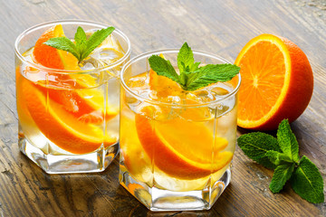 Cold drinks with ice and mint. Orange cocktail on rustic wooden