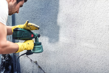 Man painting a grey wall, renovating exterior walls of house