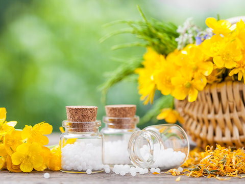 Bottles of homeopathy globules and healthy herbs in basket.
