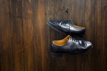 Black shoes  hanging on the nail over wooden background