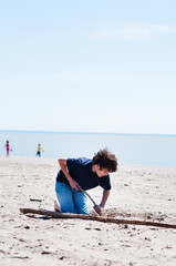 young boy using a stick to dig in the sand on a beach