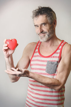 Handsome old bearded man holding red heart in his hand
