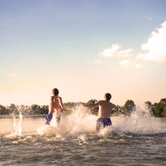Glückliche junge Menschen laufen und springen am See beim Sonnenuntergang