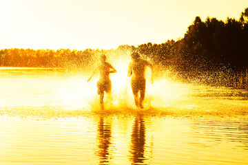 Glückliche junge Menschen laufen und springen am See beim Sonnenuntergang