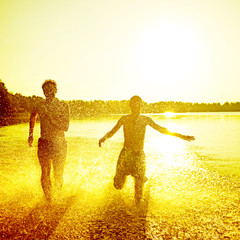 Glückliche junge Menschen laufen und springen am See beim Sonnenuntergang