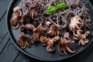 Frying pan with baby octopuses and black rice noodles, close-up