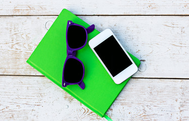 Notebook, mobile phone and sunglasses on a wooden table