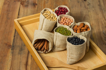 Different kinds of beans and cinnamon in sacks bag on wooden background